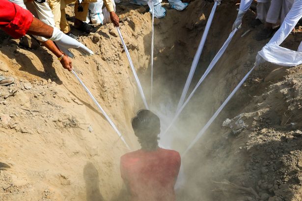 People lower the body a man who died from the coronavirus disease (COVID-19) into a grave, during his funeral at a graveyard in New Delhi, India