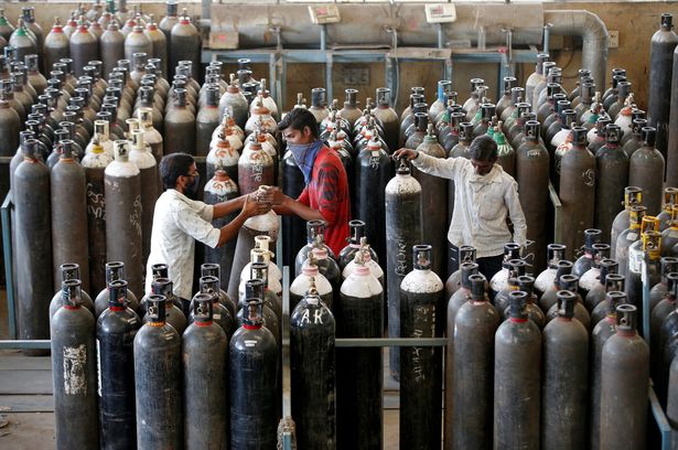 People carry oxygen cylinders after refilling them in a factory