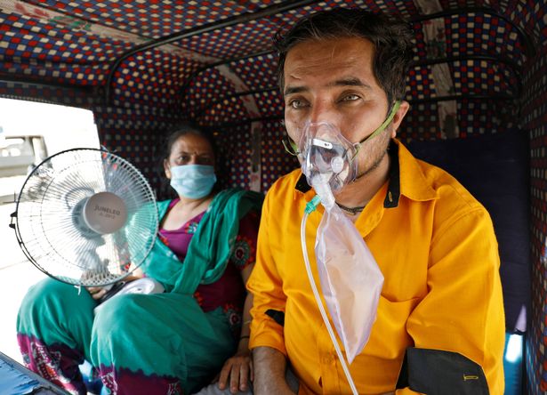 A patient wearing an oxygen mask looks on as his wife holds a battery-operated fan while waiting in an auto-rickshaw to enter a Covid-19 hospital for treatment in Ahmedabad