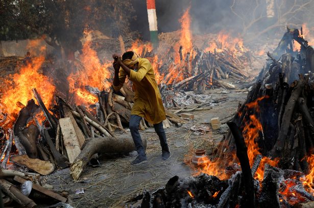 A man runs past the burning funeral pyres of those who died from coronavirus during a mass cremation, at a crematorium in New Delhi, India April 26