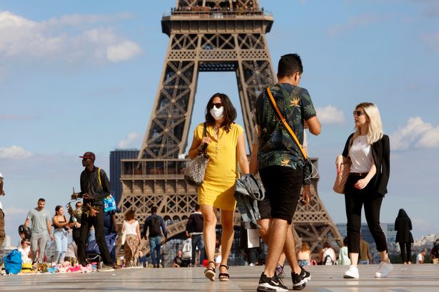 A woman with a protective mask walks in front of Eiffel Tower