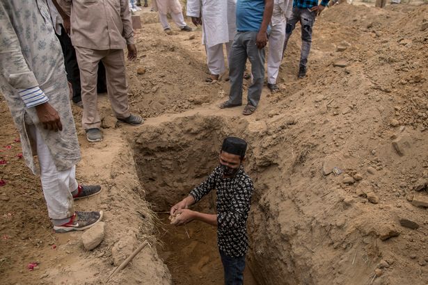 Family members and relatives prepare to bury a body of a patient who died of the Covid-19 coronavirus disease at a graveyard on April 20, 2021 in New Delhi,