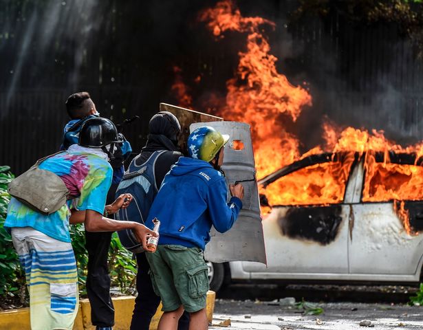 Anti-government demonstrators take cover behind shields near a burning car during clashes near Altamira Square in Caracas in 2017