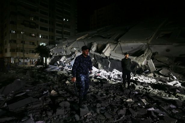 Palestinian policemen stand at the site where a building was destroyed by Israeli air strikes