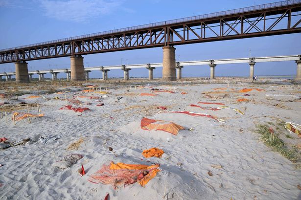 Bodies of suspected coronavirus victims are seen in shallow graves buried in the sand near a cremation ground on the banks of Ganges River