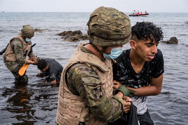 Two migrants who have just arrived swimming in Ceuta are guided to the border by the Spanish army