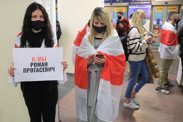 A young woman stands with a poster reading 'I am, we are Roman Protasevich' and the Belarus flag as passengers disembark from the flight from Athens after it landed at Vilnius International Airport, its initial destination