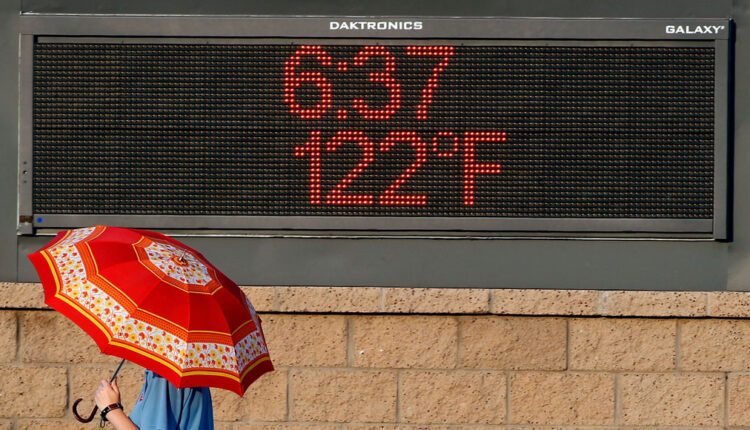 person walking by an electronic sign in Phoenix that reads 122 degrees and 6:27pm