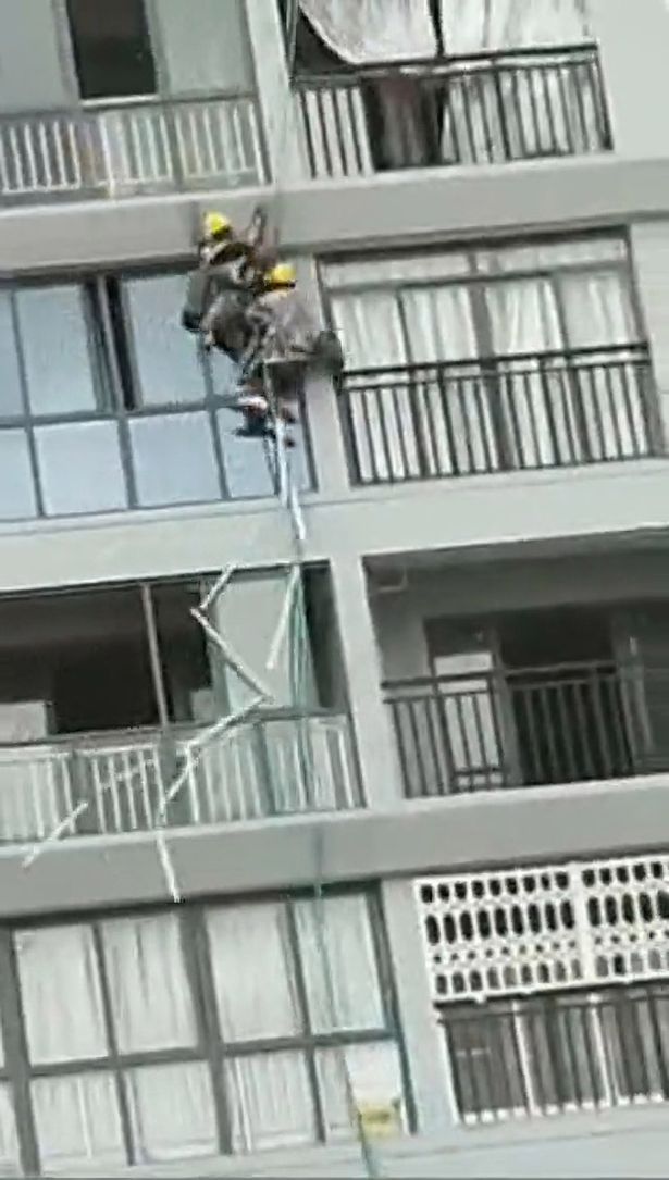 Workers in China dangle on a rope after strong winds blew them from a building