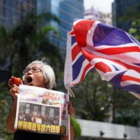 A supporter holds an apple and a copy of Apple Daily newspaper outside the court to support media mogul Jimmy Lai, founder of Apple Daily, over charges related to an unauthorized assembly on Oct. 1, 2019, in Hong Kong on Friday.  | REUTERS