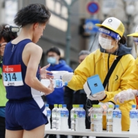 A staff member hands a face mask to a runner who finished a race during a Tokyo Olympics test event in Sapporo earlier this month. | KYODO