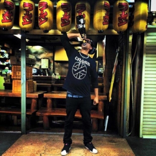 Ash Hudson poses with a big bottle of sake outside a pub in Japan. Having lived here for a while, the designer has launched a new line of T-shirts to support the 'StopAsianHate movement.