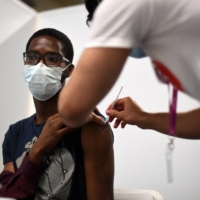 Members of the public receive a dose of Pfizer's COVID-19 vaccine at a center in London on Friday.  | AFP-JIJI