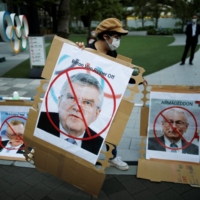 An anti-Olympics protester prepares placards with photos of Olympics officials, including IOC President Thomas Bach (center) near Olympic Rings monument outside the Japan Olympic Committee (JOC) headquarters in Tokyo on June 14. | REUTERS