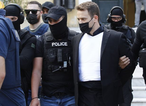 Babis Anagnostopoulos wears a bullet-proof vest as he is escorted out of a prosecutor's office by heavily-armed police