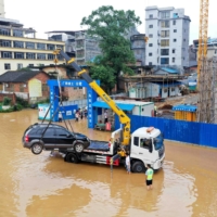 Traffic police officers work on removing a trapped vehicle with a crane from a flooded street near the swollen Rongjiang river following heavy rainfall in the region, in Rongan in China's southern Guangxi region on July 2. | CHINA DAILY / VIA REUTERS