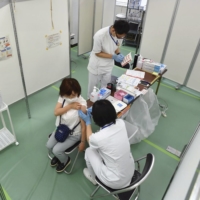 A woman is inoculated against COVID-19 at a mass coronavirus vaccination center run by the Self-Defense Forces in the Otemachi business district of Tokyo in May. | POOL / VIA KYODO 
