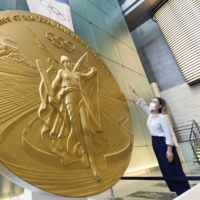 Golden opportunity: A woman stands in front of a 2.5-meter tall replica of a Tokyo Olympics gold medal at Nihonbashi Mitsui Tower in Tokyo. | KYODO
