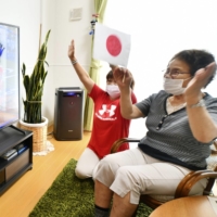 Two women cheer for the Japanese women's Olympic softball team at a public housing unit for those whose homes were destroyed in the 3/11 disasters, in Iwaki, Fukushima Prefecture, on Wednesday. | KYODO