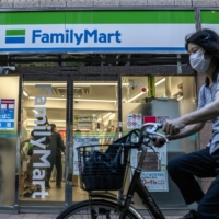 A cyclist passes a FamilyMart Co. convenience store in Tokyo in July 2020. The operator is outpacing Lawson Inc. and Seven-Eleven Japan Co. in terms of introducing labor-saving operations. | BLOOMBERG