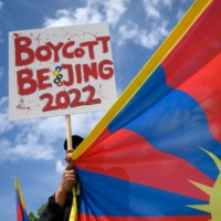 A Tibetan activist holds a placard and a Tibetan flag during a protest against the Beijing 2022 Winter Olympics in front of the Olympics Museum in Lausanne, Switzerland, on June 23. | AFP-JIJI