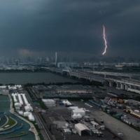 A bolt of lightning is seen in the background past the Kasai Canoe Slalom Center, the main venue for canoe slalom during the Tokyo 2020 Olympics in the capital on Sunday. | AFP-JIJI