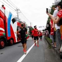 A sponsor truck and staff lead the relay before the runners' arrival during the first day of a Tokyo 2020 Olympic torch relay in Saitama Prefecture, in the city of Wako. | REUTERS