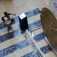 A man wearing a protective mask takes picture of a large-scale reproduction of a Tokyo 2020 Olympic medal at Nihonbashi Mitsui Tower in the capital on Wednesday. | REUTERS