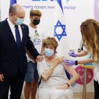 Israeli Prime Minister Naftali Bennett stands by while his mother, Mirna Bennett, receives a third dose of  a COVID-19 vaccine in Haifa, Israel, on Tuesday.  | POOL / VIA REUTERS