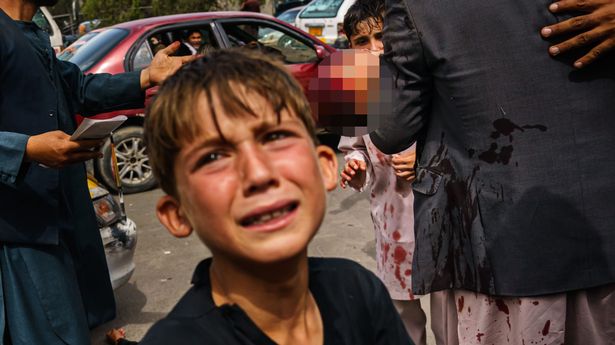 A small boy sobs as a man carries a bloodied child behind him in Kabul, after Taliban fighters used guns, whips and sticks to control the desperate crowds outside the airport