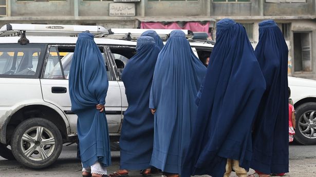 Afghan women in burqas gather next to a local taxi in Kabul July 31