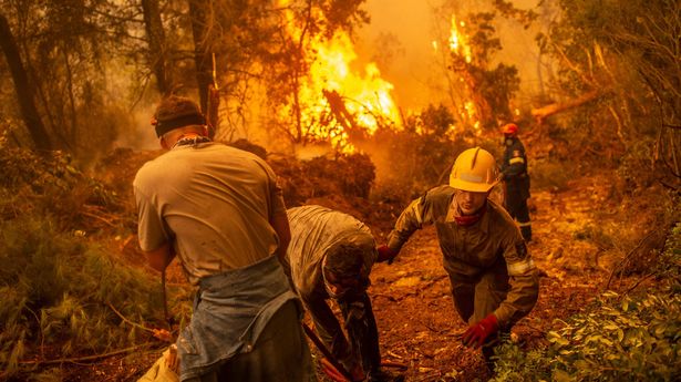 Firefighter and volunteers use a water hose near a burning blaze trying to extinguish a fire in the village of Glatsona on Evia