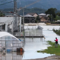 A man looks at a flooded area after heavy rainfall in Tosu, Saga Prefecture, on Sunday. | REUTERS