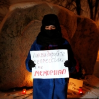 A supporter of the human rights group International Memorial stands with a placard at the Solovetsky Stone memorial after Russia's Supreme Court ruled that International Memorial must be liquidated for breaking the law on foreign agents, in Saint Peterburg on Dec. 28. The placard reads: 'Liquidate repression, not Memorial.' | REUTERS