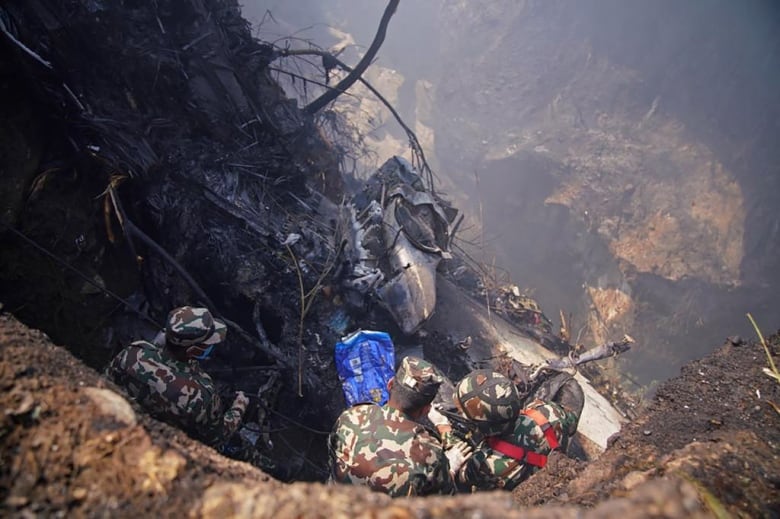 Men look down at plane wreckage at the side of a gorge.