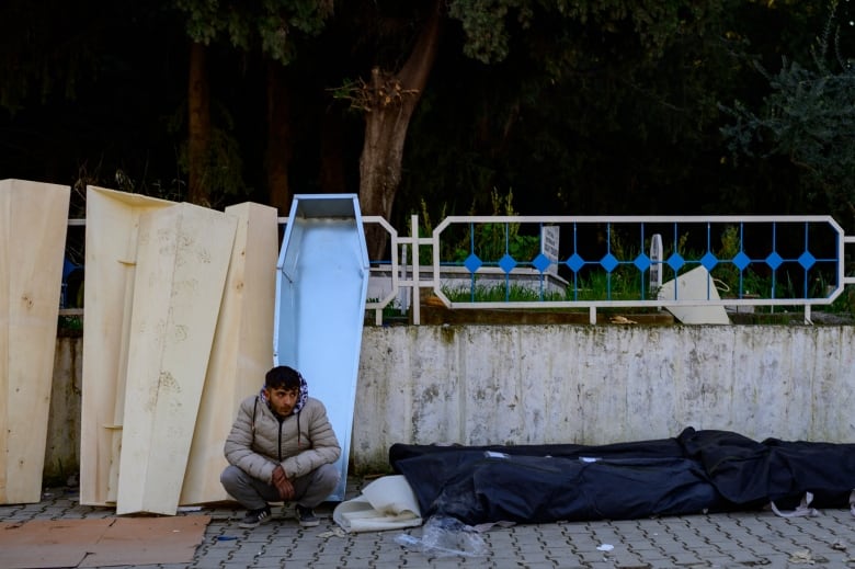 A man on his haunches before an empty casket.