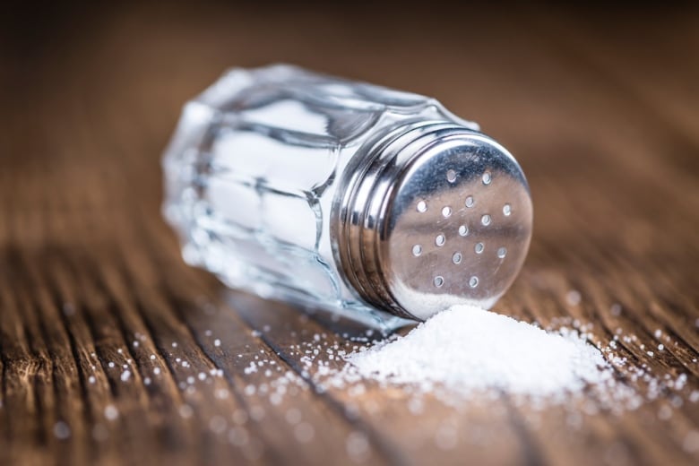 Salt shaker spilling onto wooden table.