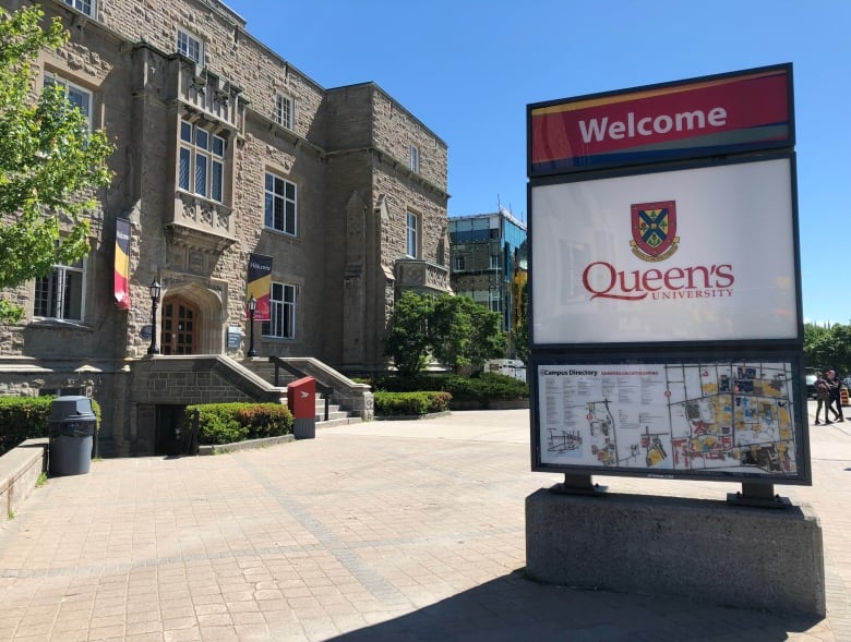 Exterior photo of a Queen's University sign with a campus building in the background
