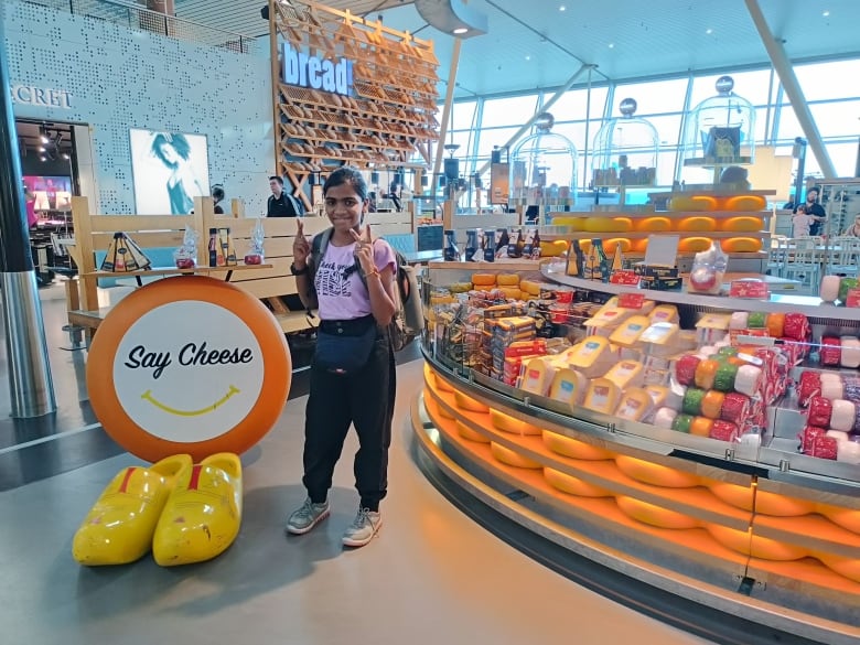 A girl flashes the peace sign next to a sign that reads 'Say Cheese.'