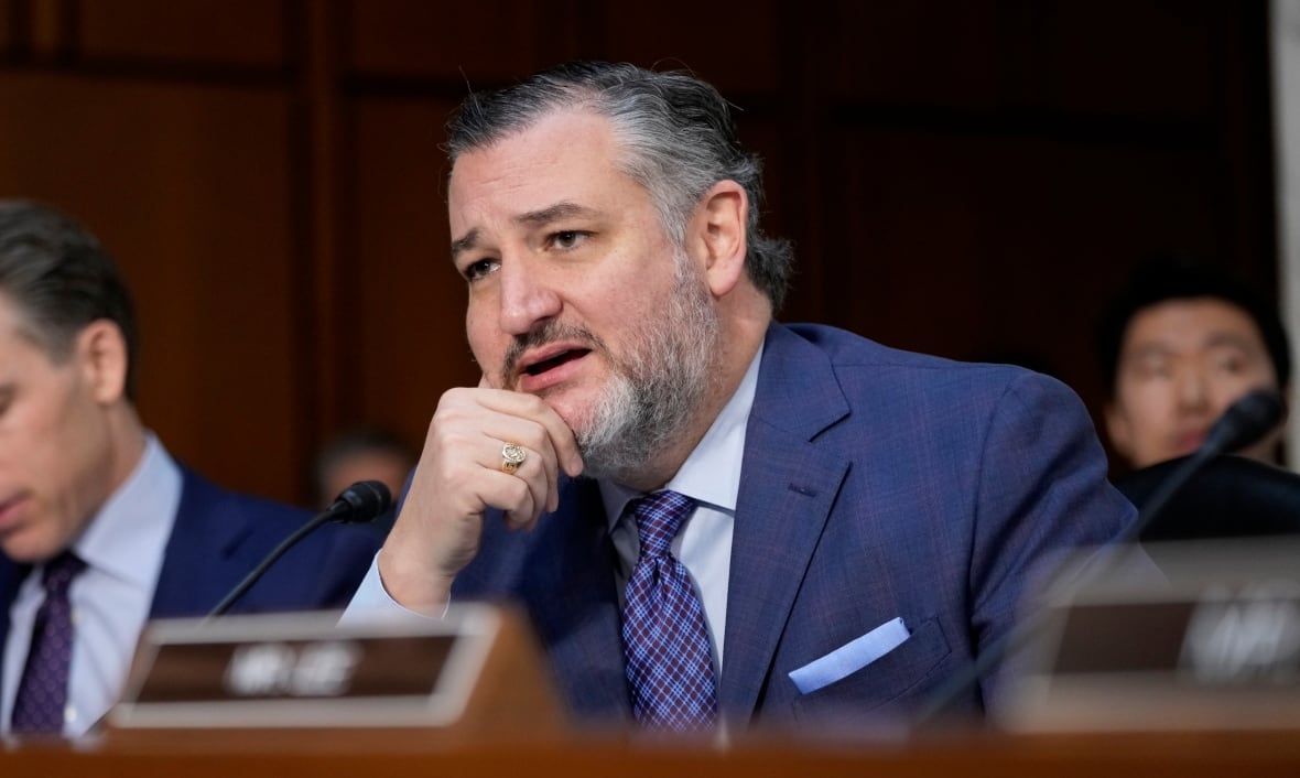 A man in a suit speaks while sitting in front of a microphone.