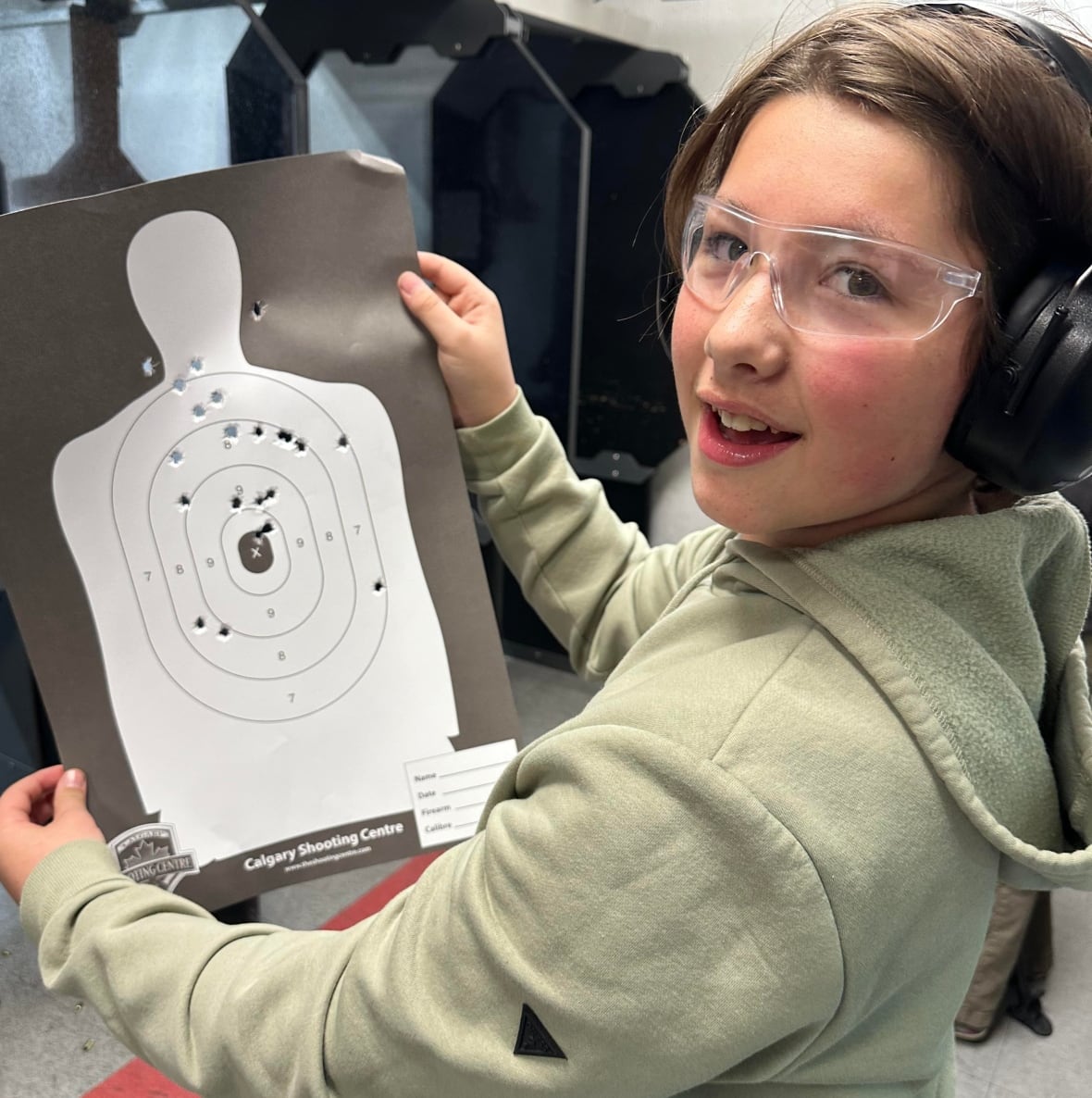A teen boy holds up a paper target full of bullet holes.