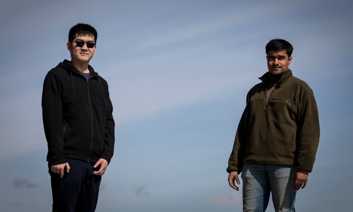 Two young men stand against a blue sky