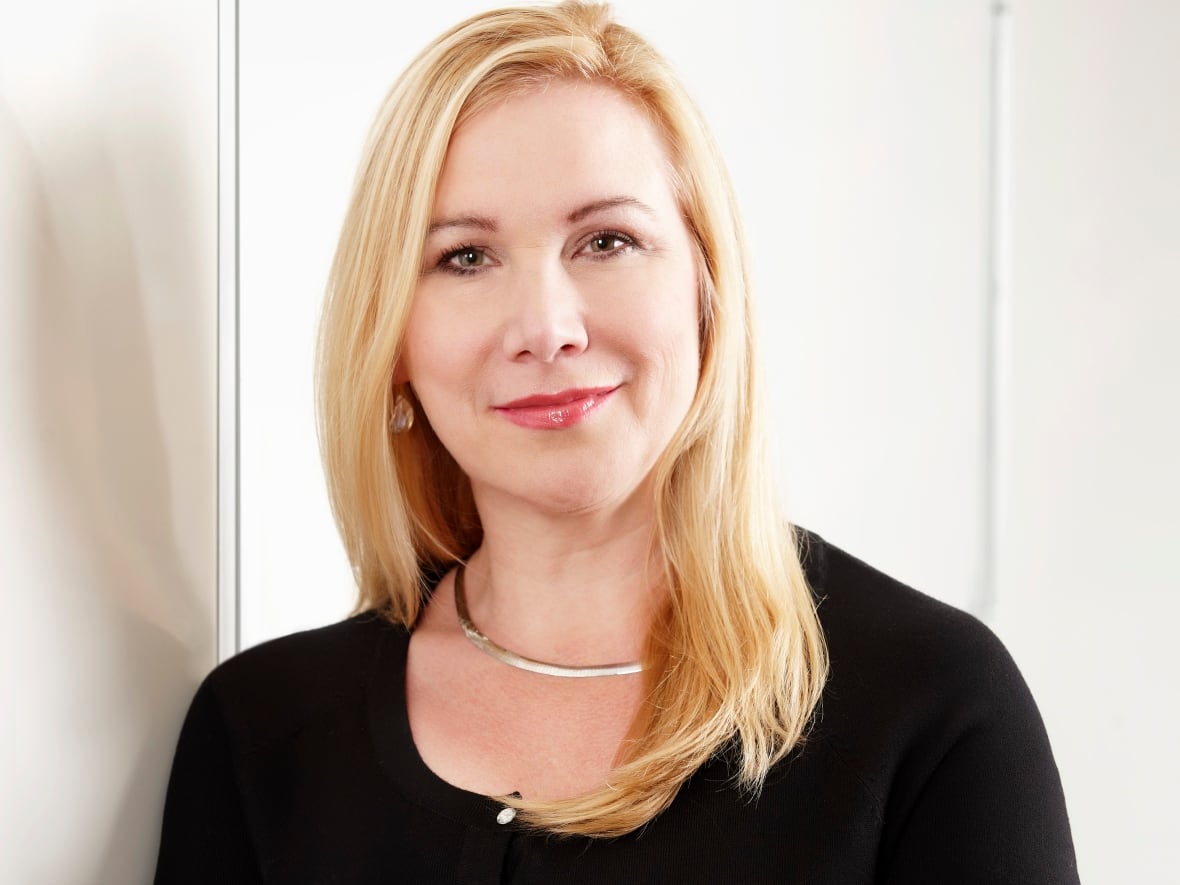 A woman with long blond hair wears a black sweater.