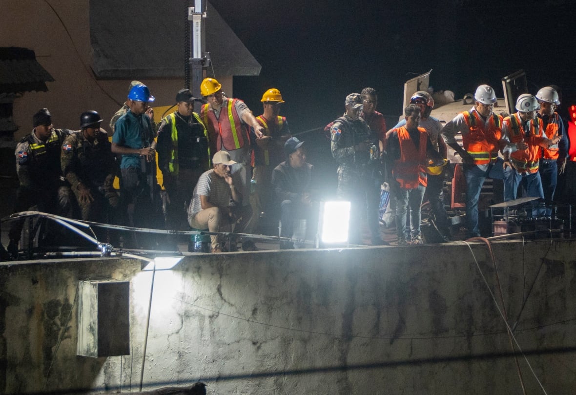 Rescue workers stand in front of a collapsed building.