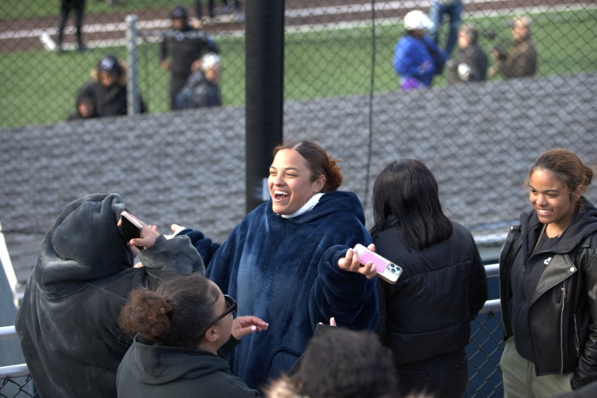 A young woman holding a cellphone is smiling at the New Jersey baseball game.