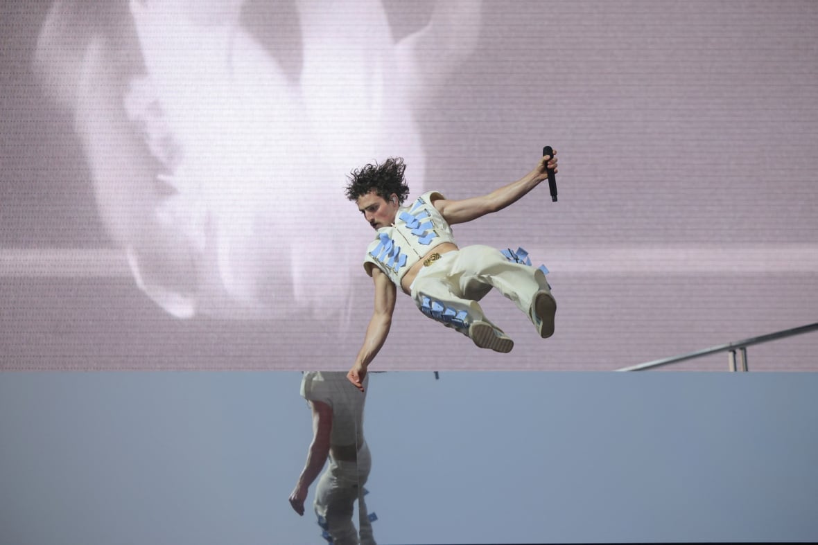 A male musician doing a flip off a stage while holding onto his mic.