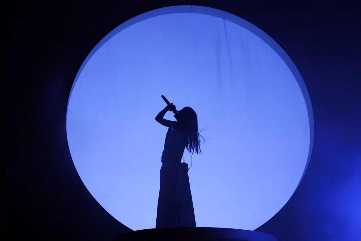 A woman backlit singing on stage with a large circle cutout lit in blue.