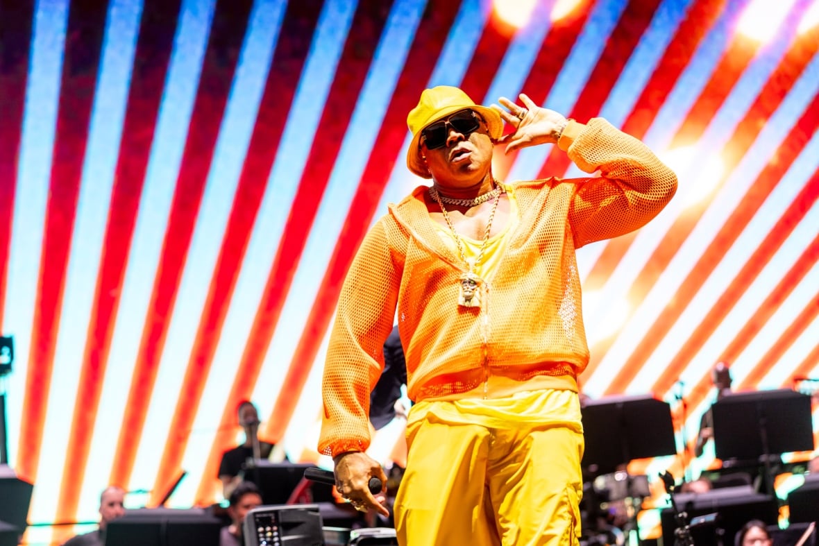 A male Black rapper performing on stage with musicians behind him.