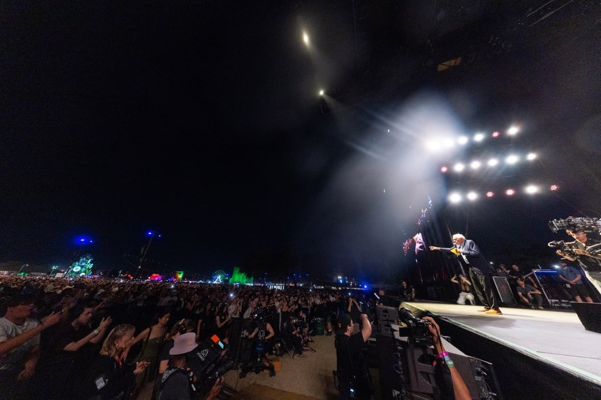 Bernie Sanders on stage speaking to a packed outdoor crowd at night.