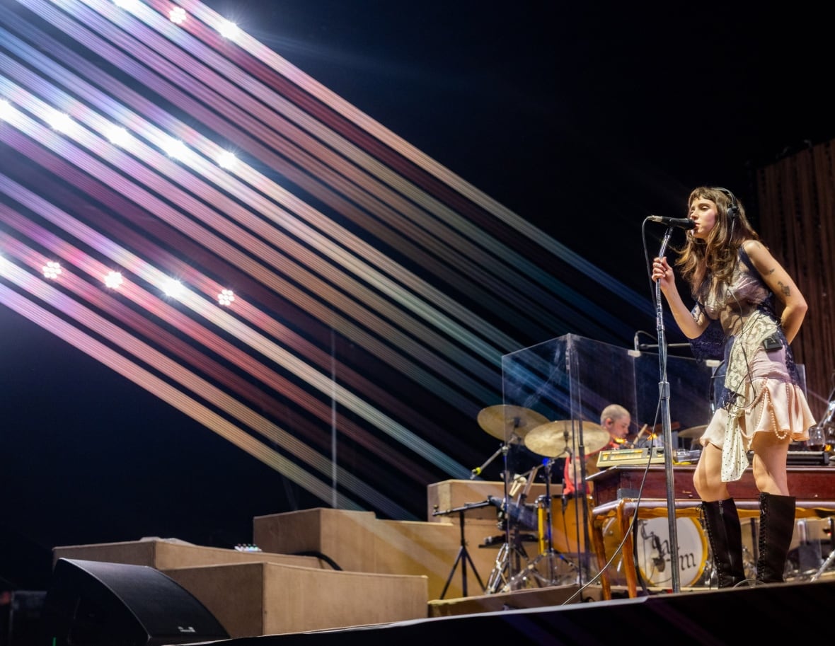 A female singer performing on stage at a mic, with other musicians behind her.